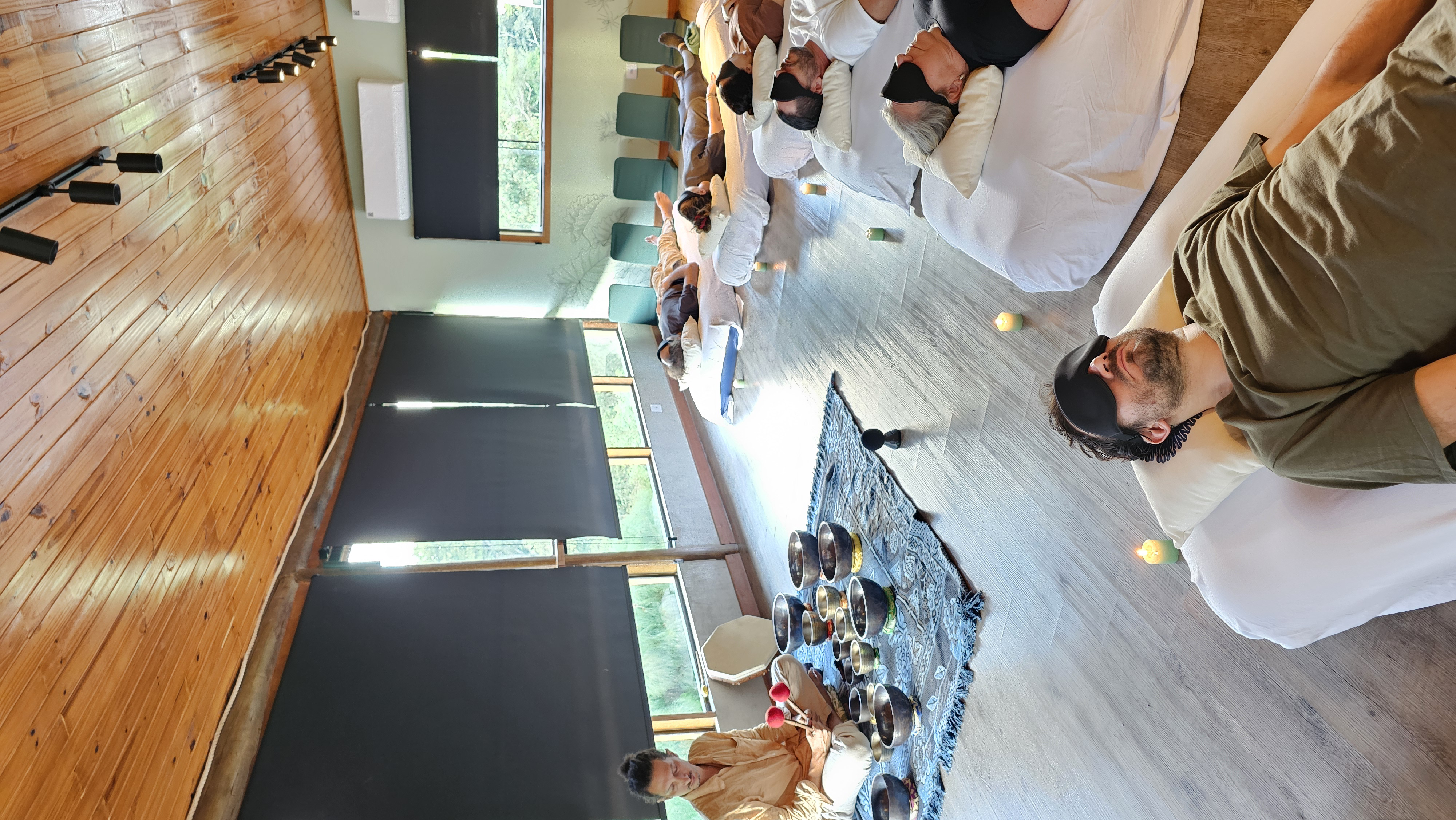 Participantes deitados em futons enquanto facilitadora conduz banho sonoro com tigelas.