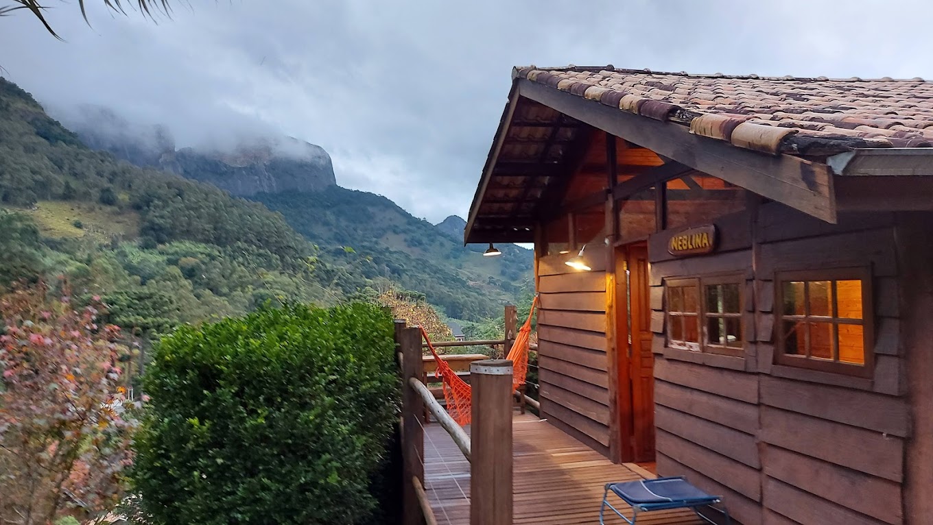 Interior do chalé com lareira de pedra, cozinha e madeira natural
